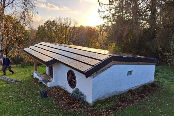 Petit bâtiment blanc dans un jardin avec un toit en tuiles solaires