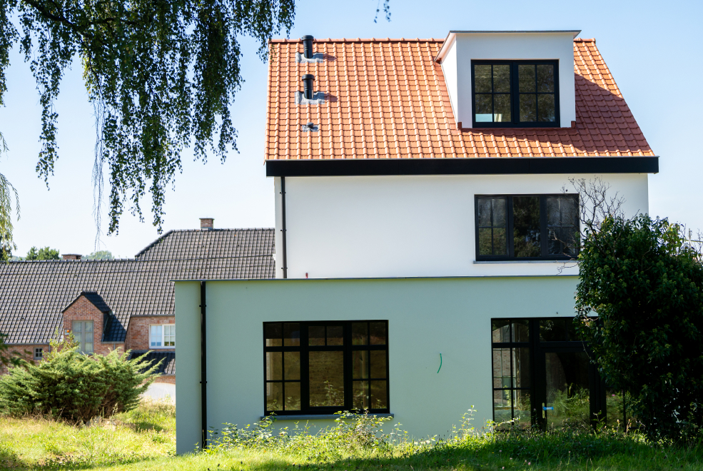 Maison à étages avec une façade en crépi blanc sur isolant, châssis foncés et toit en tuiles rouges
