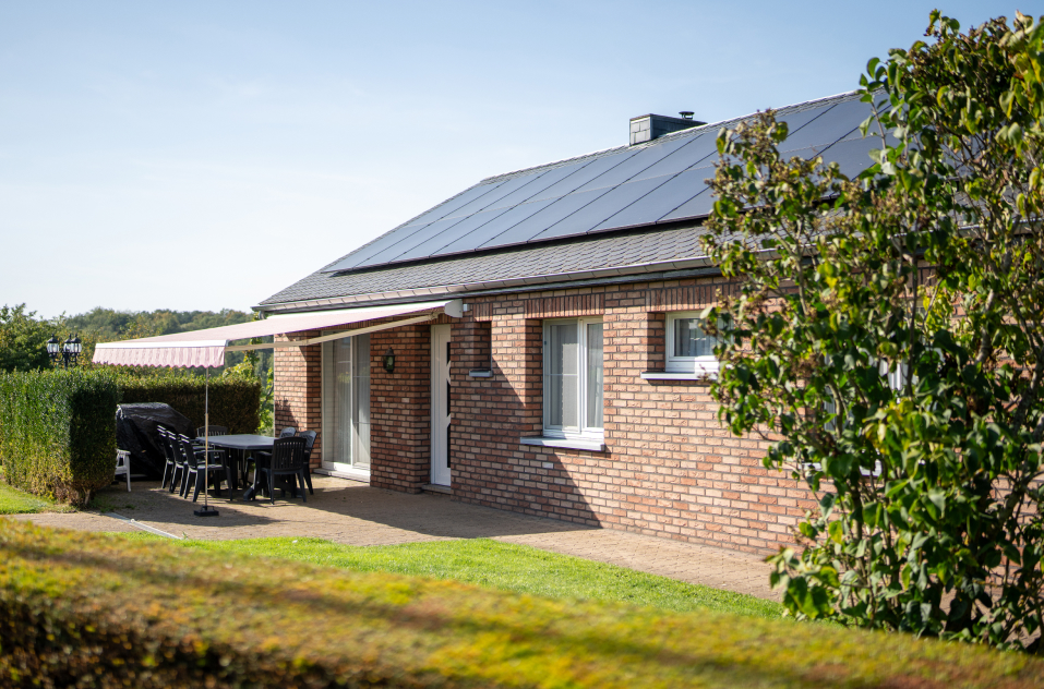Maison plain-pied avec une façade en briquettes et la toiture équipée de panneaux photovoltaïques