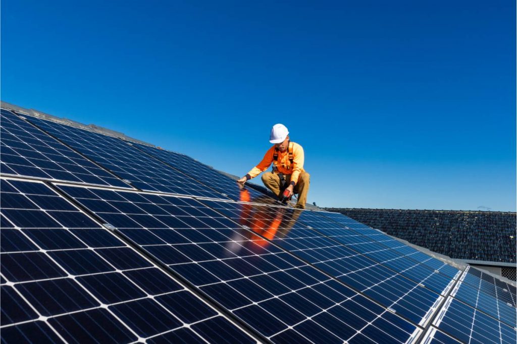 Ouvrier en orange sur un toit en train de poser des panneaux photovoltaïques
